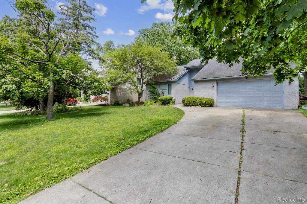 View of front of house with a front lawn, concrete driveway, a garage, brick siding, and a shingled roof