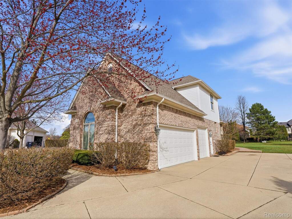 View of front facade with brick siding, driveway, a shingled roof, and an attached garage