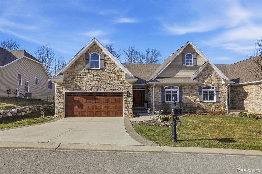 View of front of home with stone siding, a front lawn, and driveway