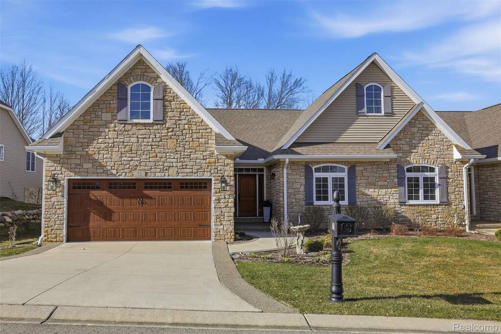View of front of property with stone siding, a front yard, driveway, and a shingled roof