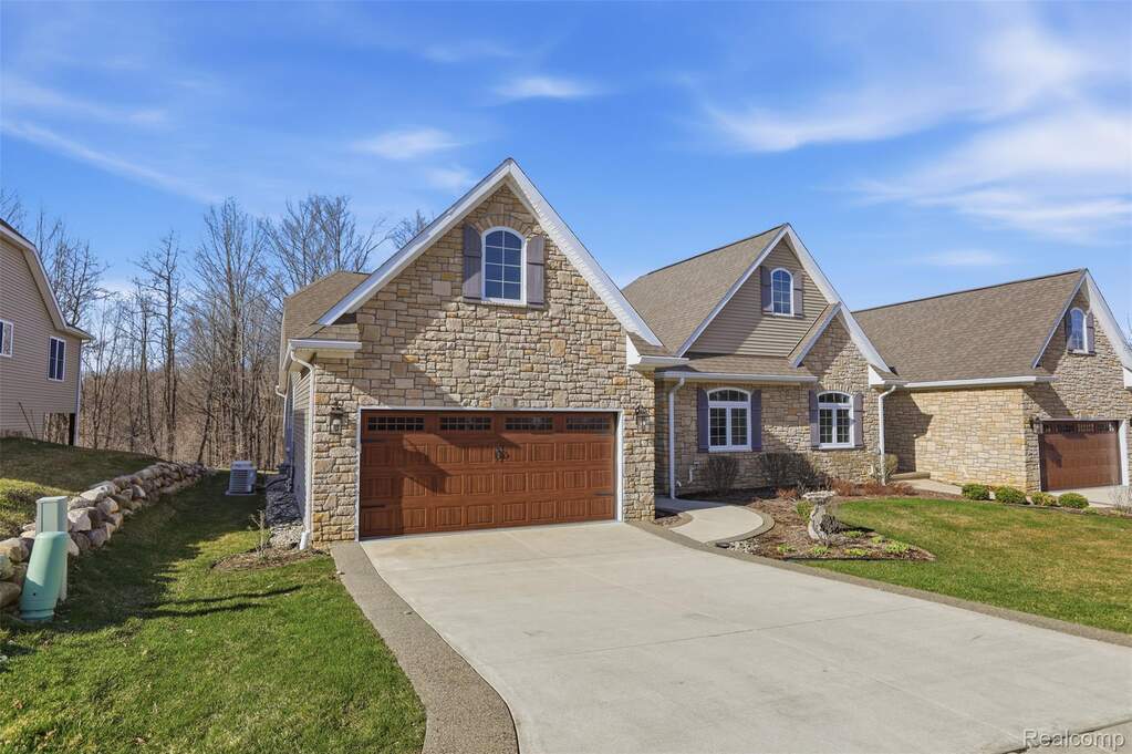 View of front of property featuring stone siding, a front lawn, driveway, and roof with shingles