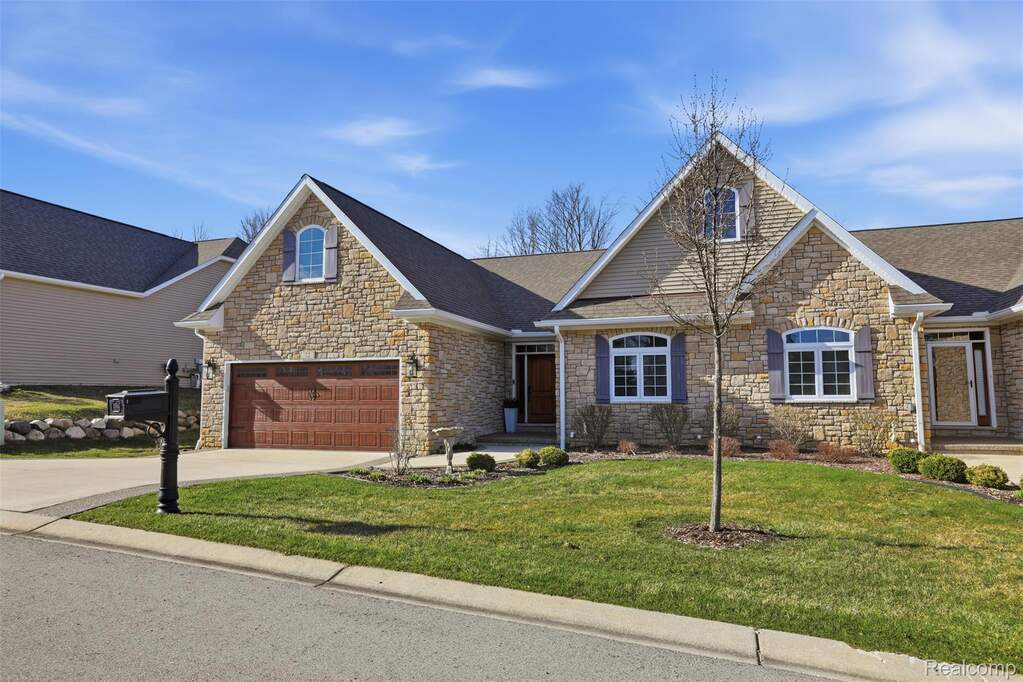 View of front of property featuring stone siding, driveway, a front lawn, and a shingled roof