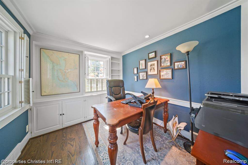 Office area with dark wood-type flooring, crown molding, and built in shelves