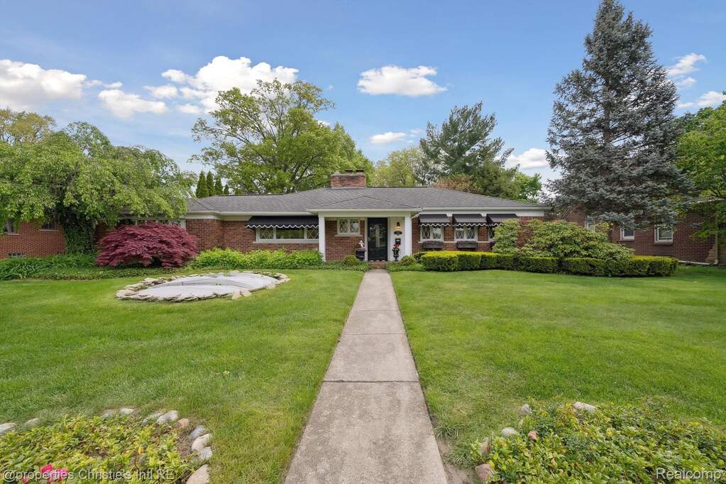 View of front of home featuring a front yard, a chimney, covered porch, and brick siding