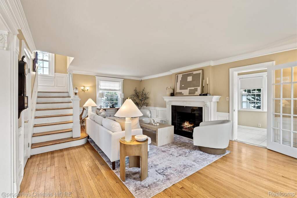Living room with light wood-type flooring, a lit fireplace, crown molding, and a wainscoted wall
