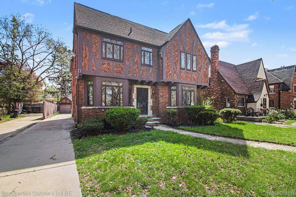 Tudor house with brick siding, a chimney, and a front yard