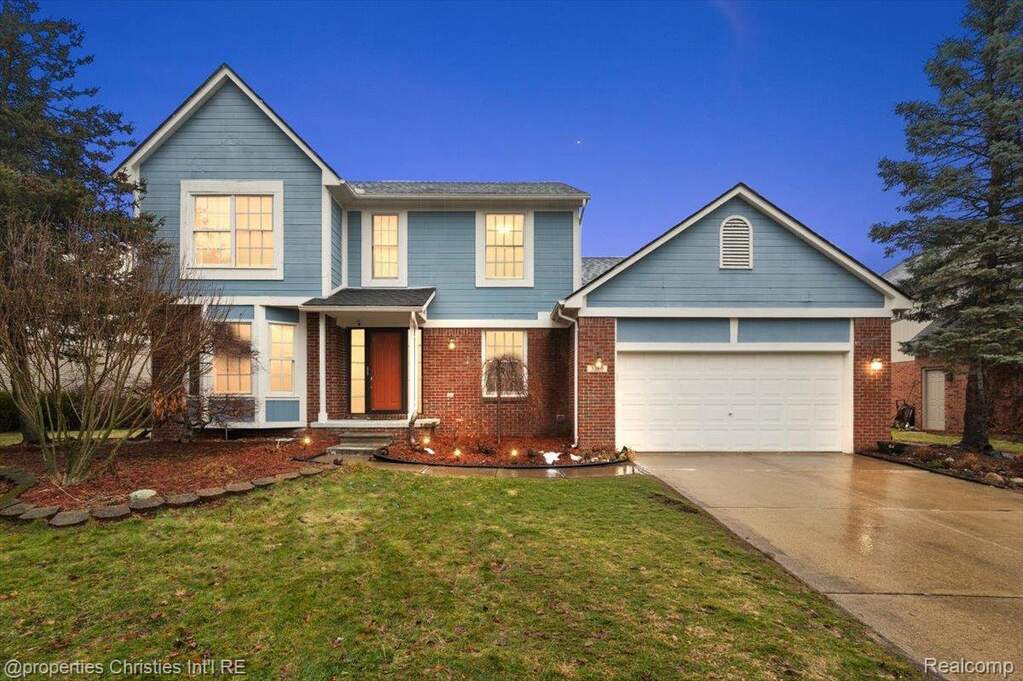 Traditional-style home featuring driveway, brick siding, an attached garage, and a front yard