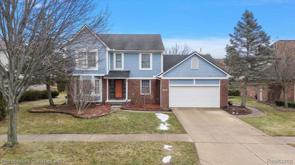 Traditional-style house featuring concrete driveway, brick siding, a front yard, and a garage