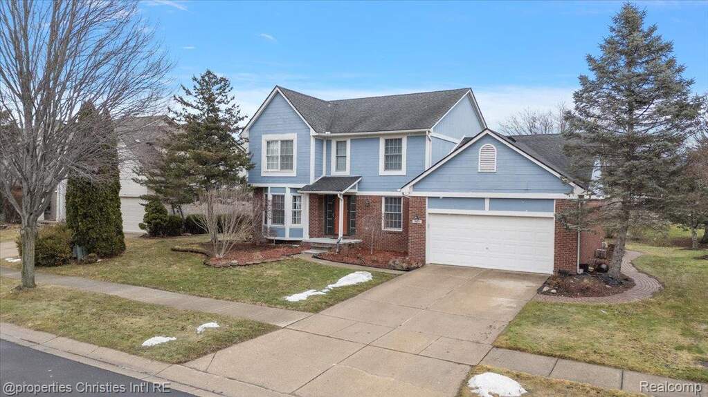 Traditional home featuring concrete driveway, brick siding, a front yard, and an attached garage