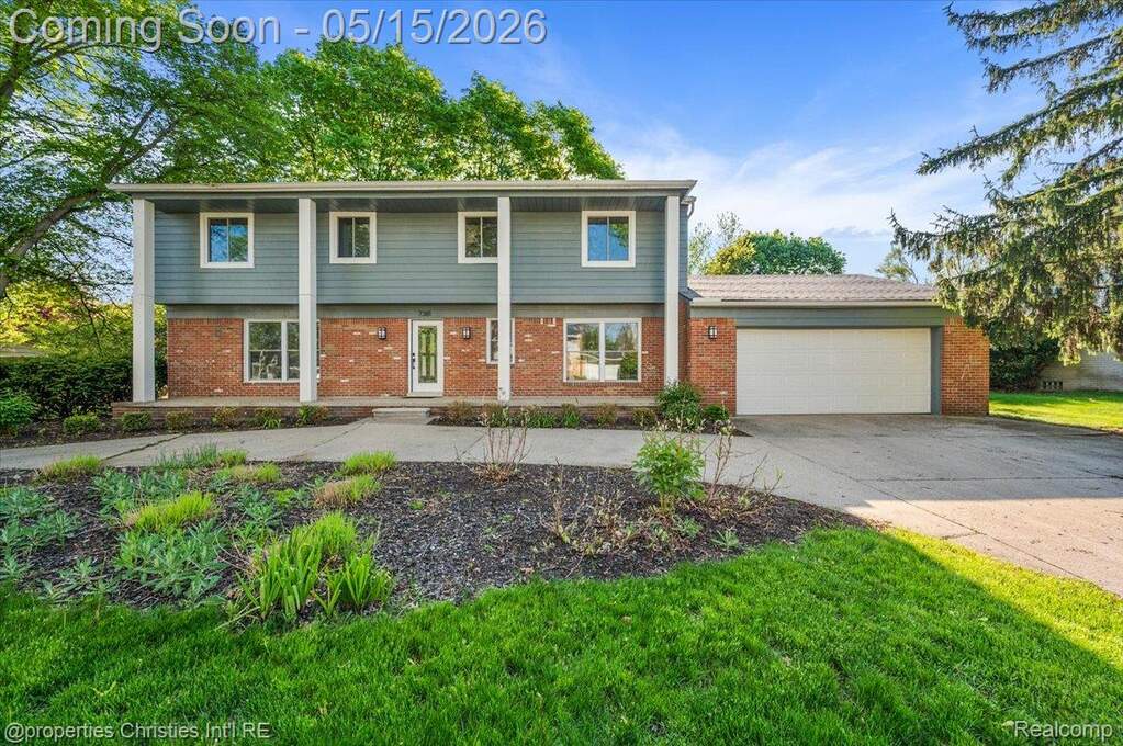 Colonial home with an attached garage, driveway, brick siding, and covered porch