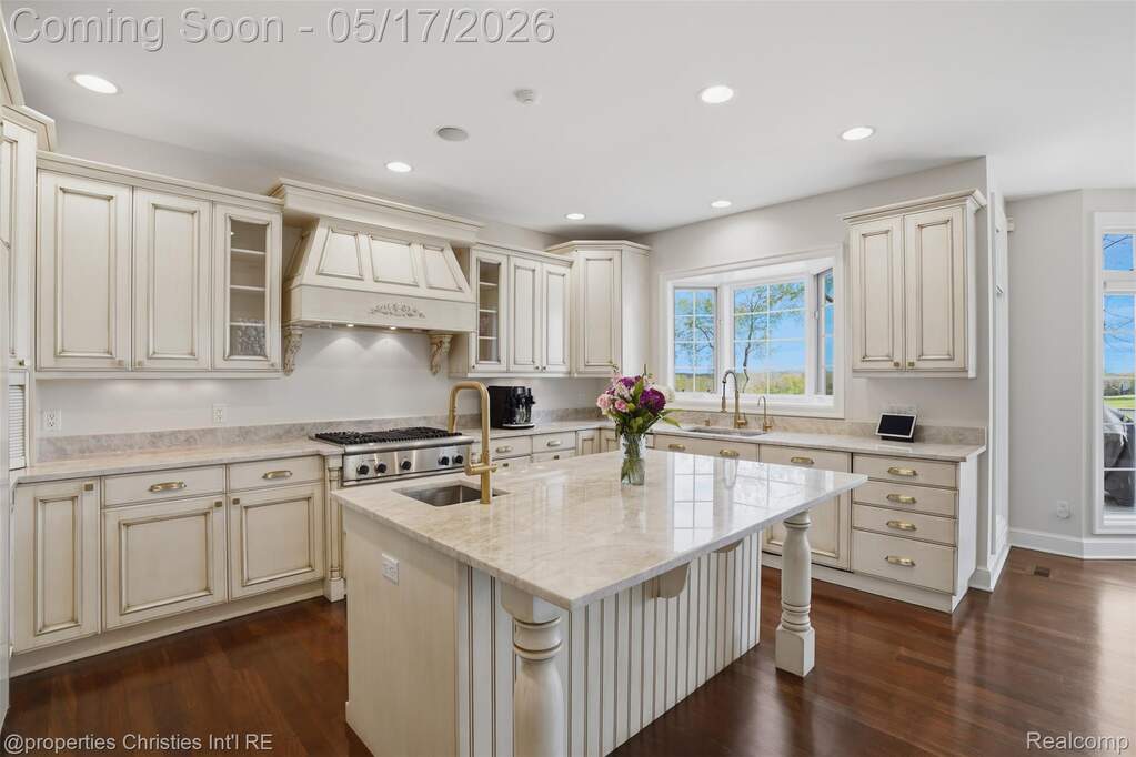 Kitchen with cream cabinetry, light stone countertops, glass fronted cabinets, a center island with sink, and dark wood finished floors