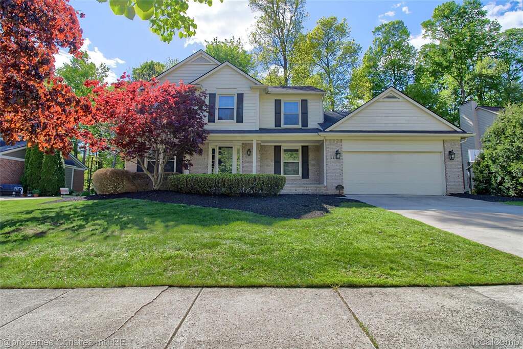 Traditional-style house with brick siding, an attached garage, a porch, driveway, and a front lawn