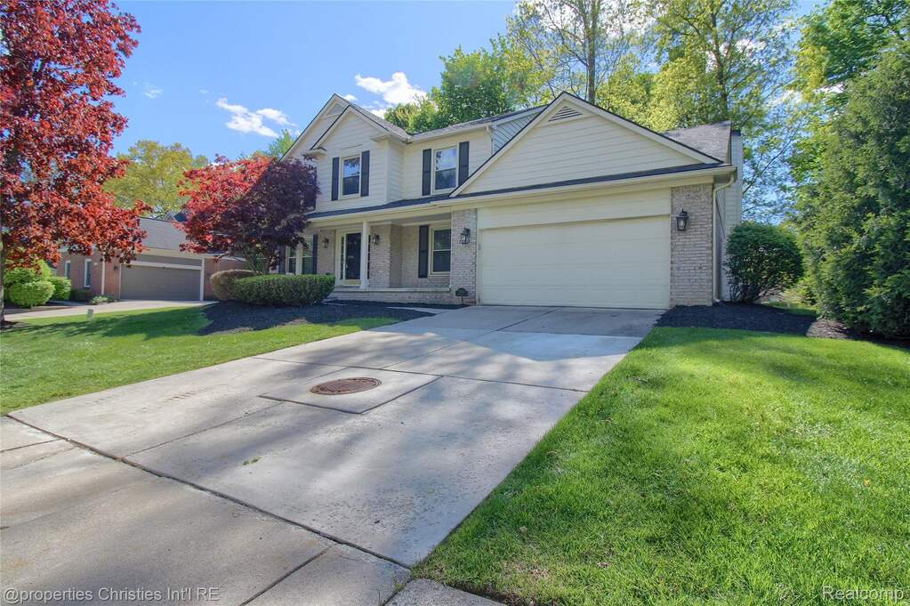 Traditional-style house featuring an attached garage, brick siding, a front lawn, concrete driveway, and covered porch