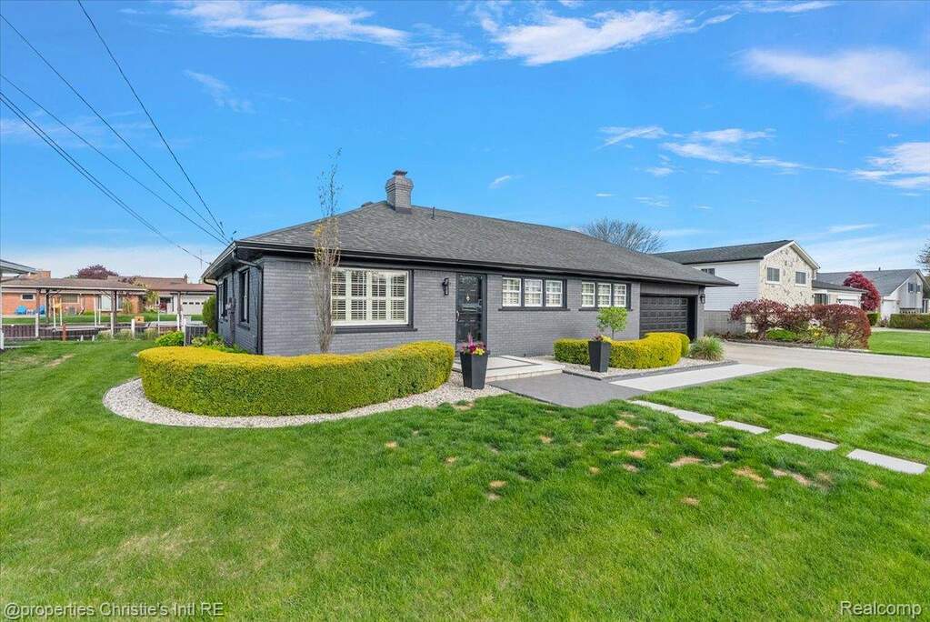 Ranch-style house featuring brick siding, a front lawn, an attached garage, a chimney, and driveway