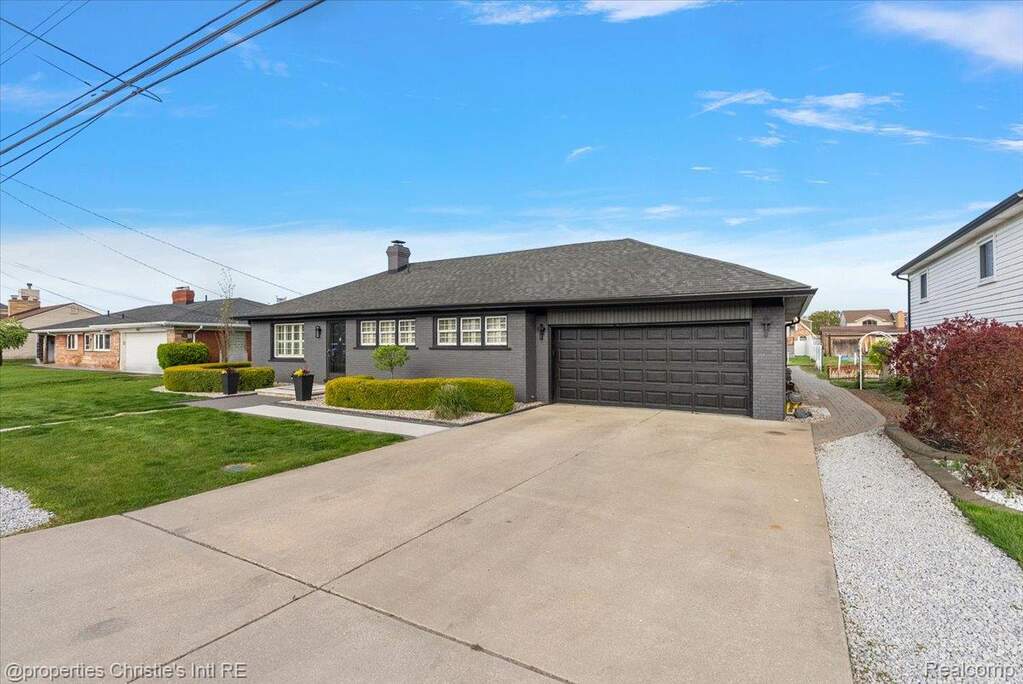 Ranch-style home featuring driveway, a garage, a chimney, brick siding, and a front yard