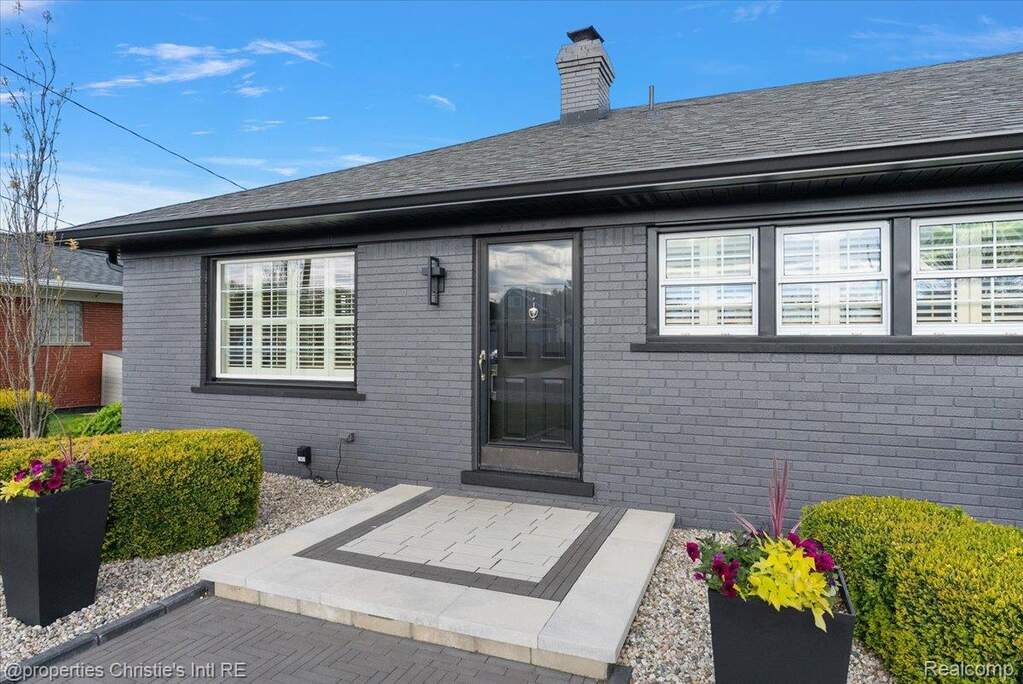 Property entrance with brick siding, a chimney, a patio area, and roof with shingles