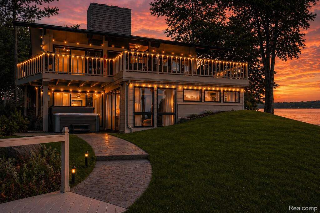 Back of house at dusk featuring a hot tub, a chimney, a balcony, and a lawn