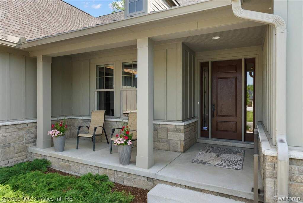 Inviting covered porch featuring a solid wood entry door with sidelights, board and batten siding, stone veneer accents, and a concrete floor