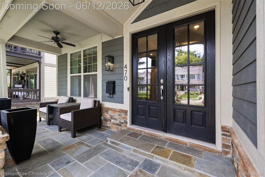 Front entry featuring double dark-paneled doors with glass inserts, a slate tile porch, stone veneer siding, and a covered porch with a ceiling fan