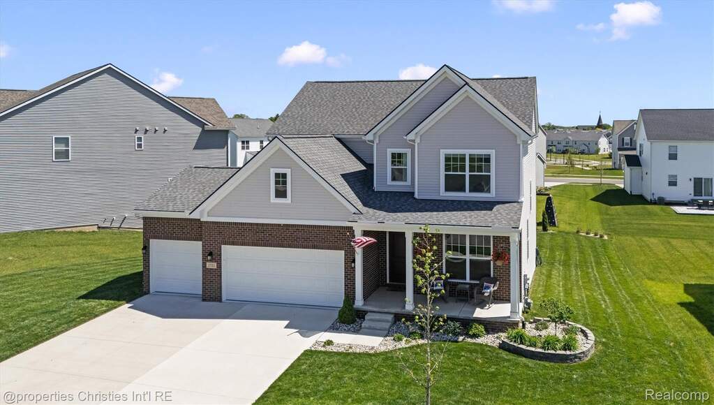 View of front of home featuring a porch, a front lawn, concrete driveway, roof with shingles, and brick siding