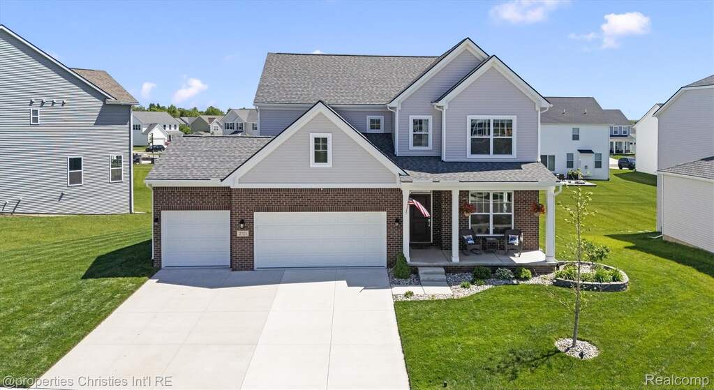 Traditional-style home featuring a porch, a front lawn, concrete driveway, and brick siding