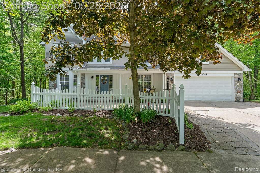 View of front of home with a fenced front yard, concrete driveway, an attached garage, a porch, and stone siding