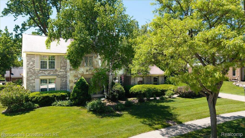 Two-story brick and stone exterior residence featuring an arched portico entryway, multiple white-framed windows with louvered shutters, and a prominent front-facing gable roof