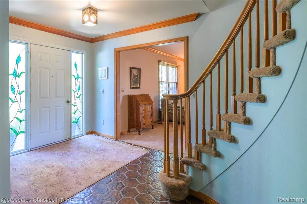 Inviting entryway featuring a paneled front door with decorative sidelight windows, a curved staircase with carpeted treads, hexagonal tile flooring, and wood trim detailing