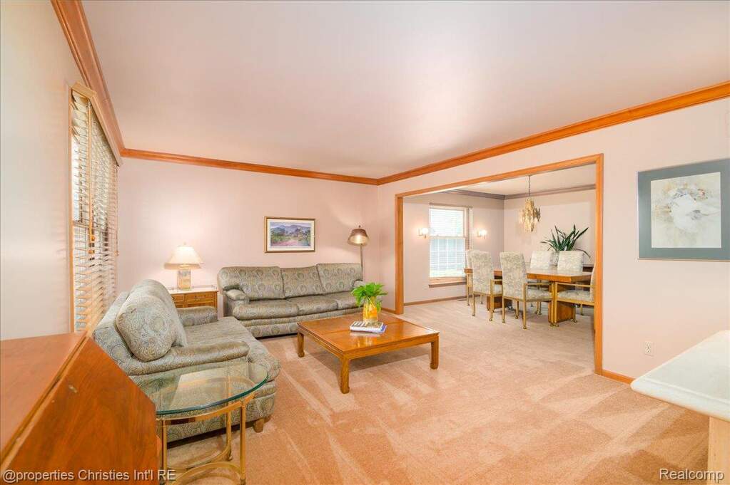 Carpeted living area with wood trim, a wide window with blinds, and a doorway opening to a dining space