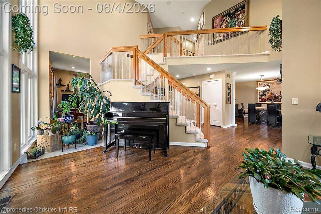 Two-story foyer featuring hardwood flooring, a grand staircase with wood railings and carpeted treads, a second-story landing, and a dining area beyond
