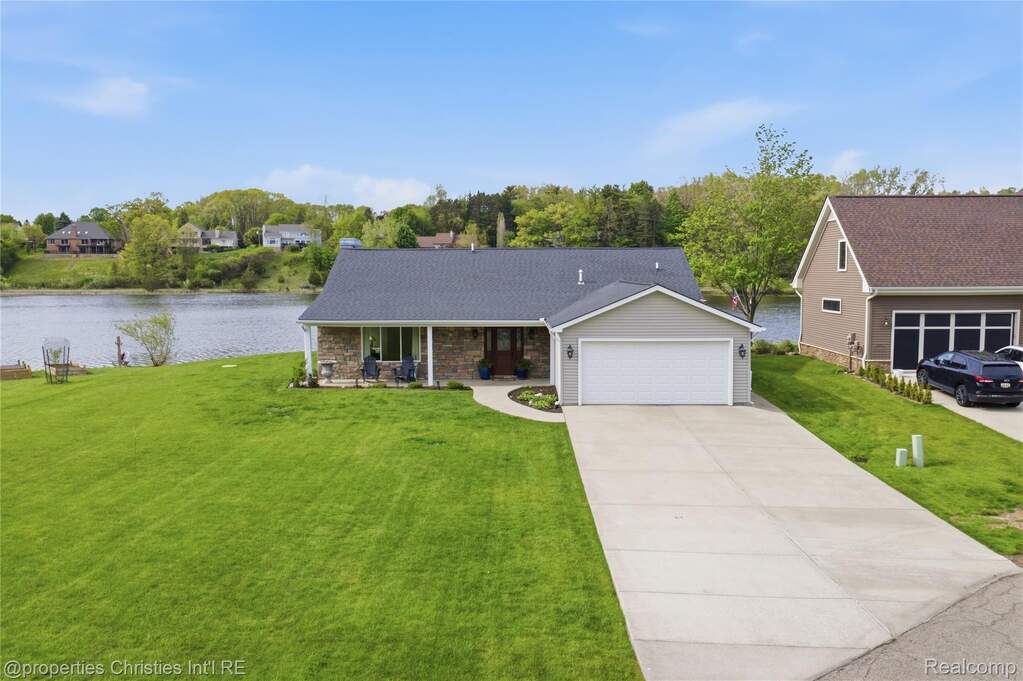 View of front facade with a front yard, covered porch, stone siding, concrete driveway, and a water view