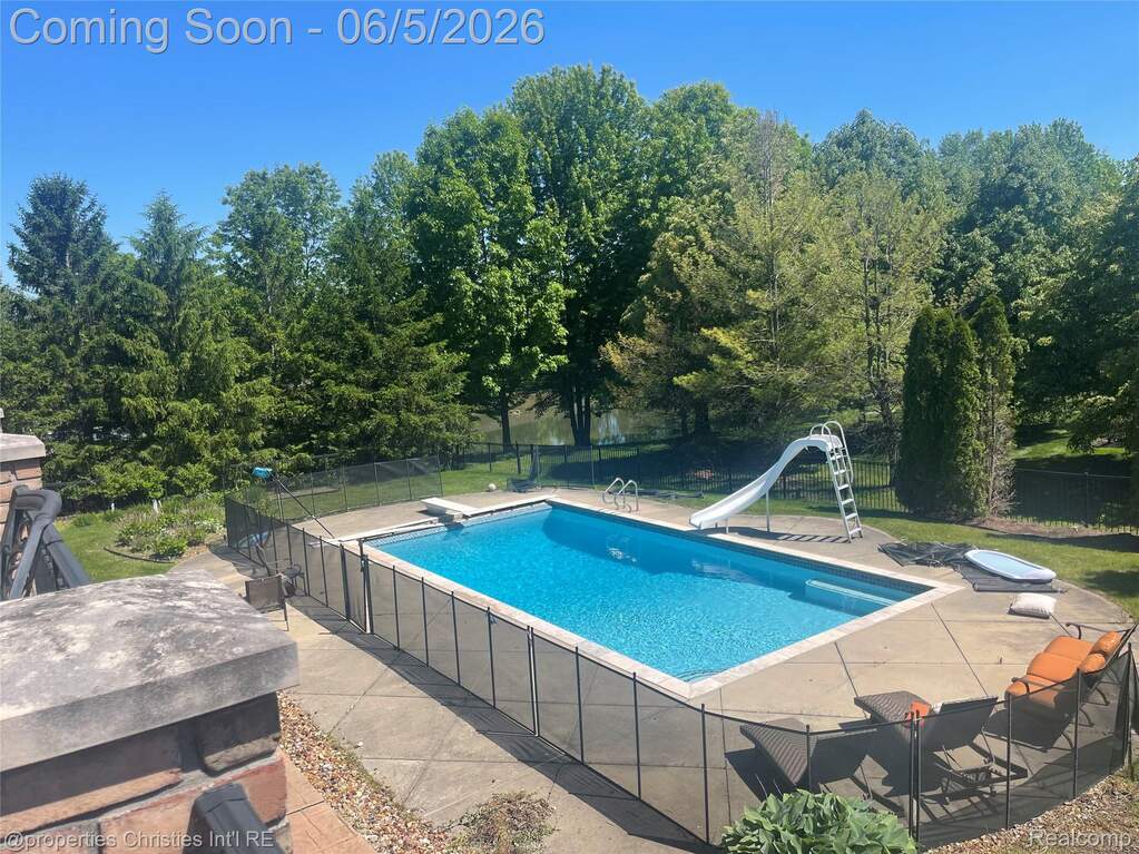 Rectangular inground swimming pool with a surrounding concrete patio, safety fencing, and mature tree-lined perimeter