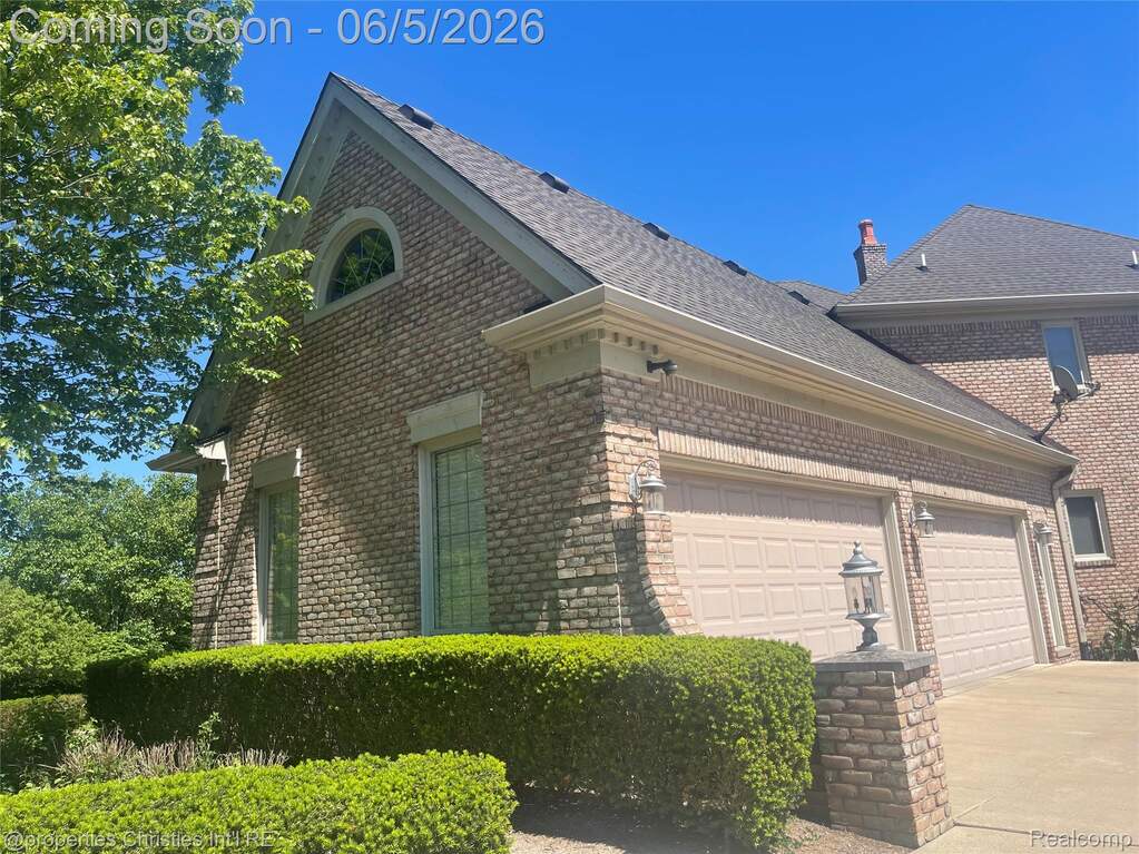 Brick exterior featuring a two-car garage with carriage-style doors, decorative sconces, and a complementary brick pillar with an outdoor light fixture