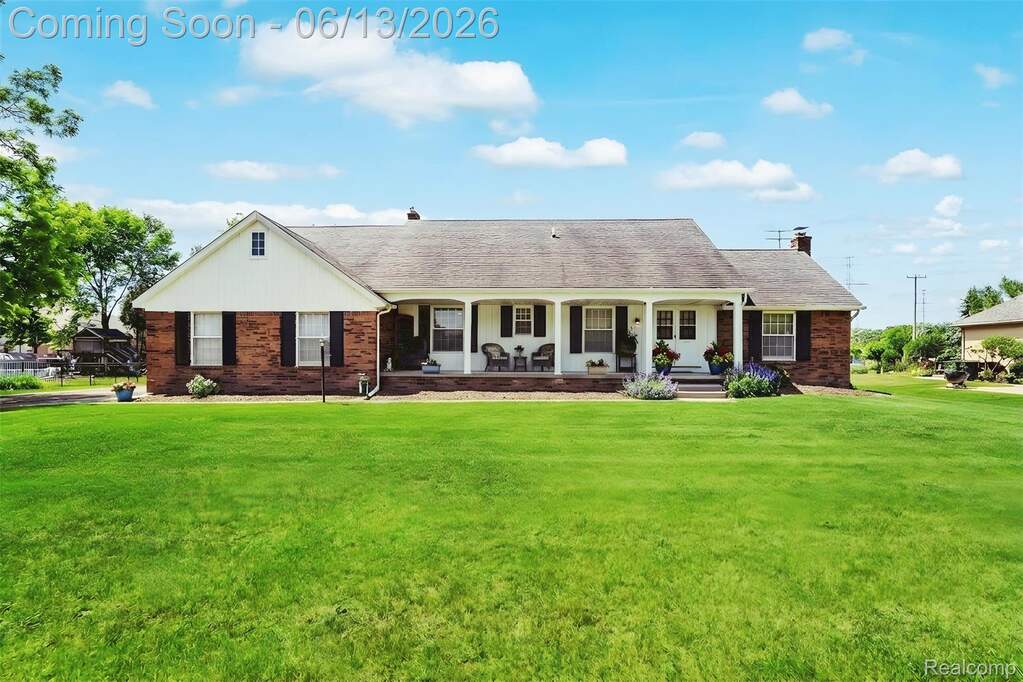 Ranch-style residence featuring a brick facade, white siding, a full-width front porch with columns, a shingled roof, and a broad green lawn