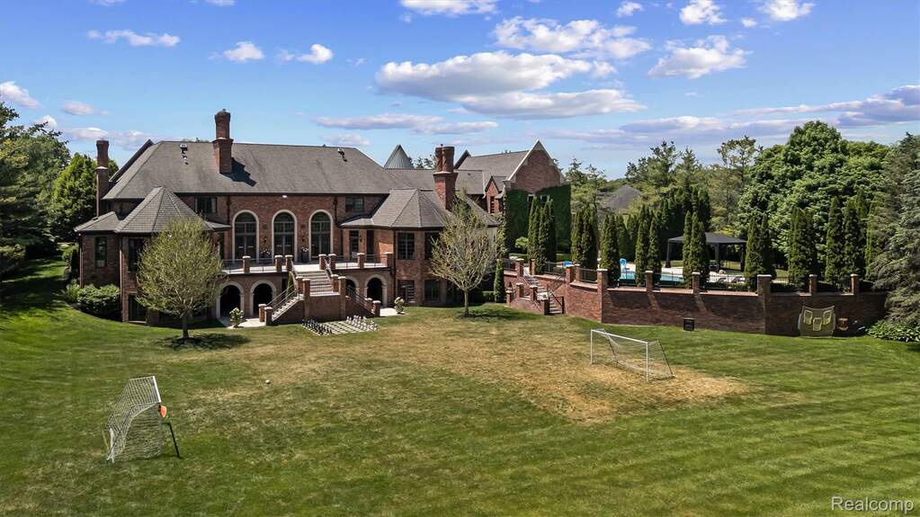 Grand brick estate featuring multiple chimneys, a multi-level rear patio, and arched windows