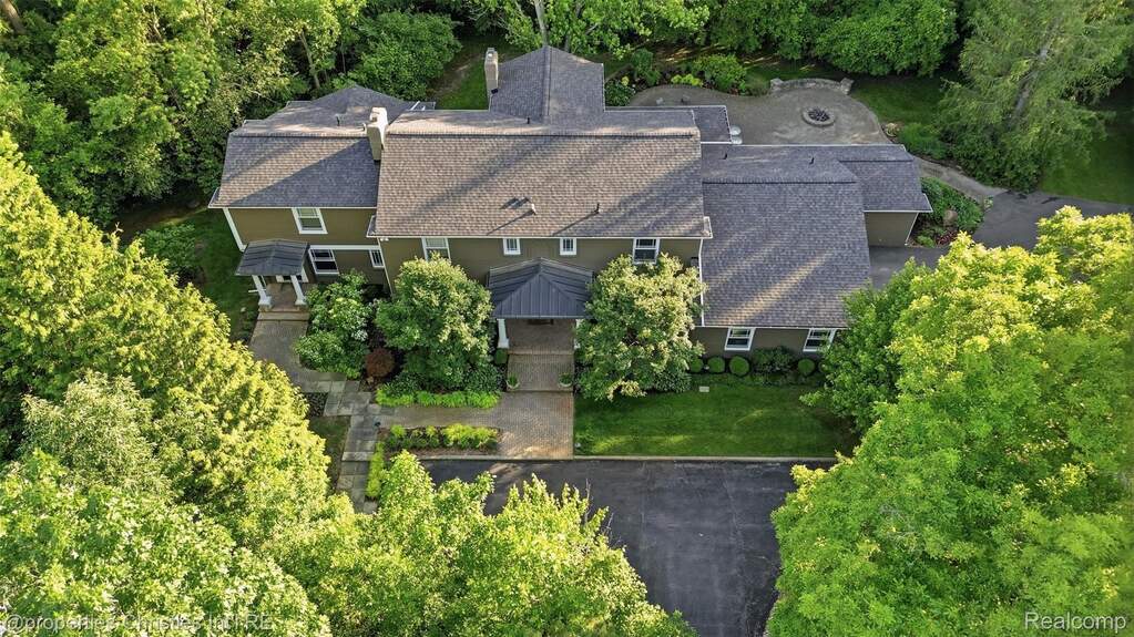 Expansive property featuring a multi-level architectural style, a large paved driveway, extensive mature landscaping, a stone patio, and a dedicated fire pit area