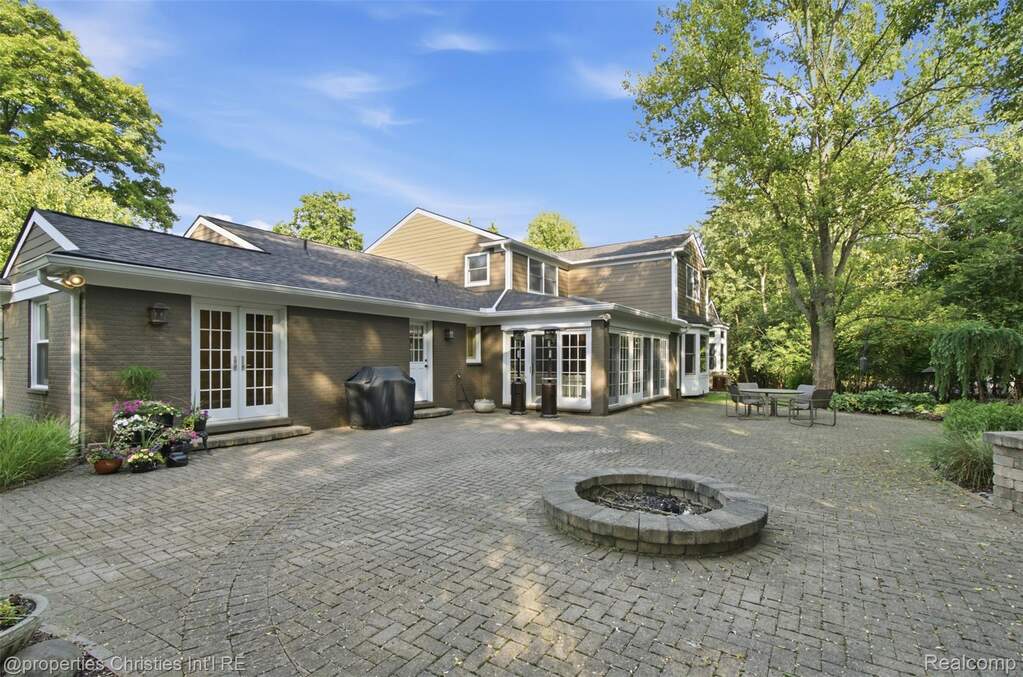 Expansive brick paver patio featuring a built-in stone fire pit, multiple sets of French doors, and a sunroom with large windows