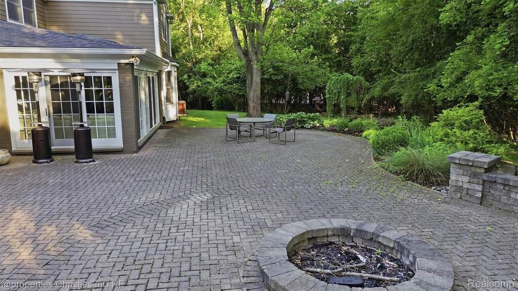 Expansive paver patio featuring a herringbone pattern, an integrated stone fire pit, and a stone retaining wall