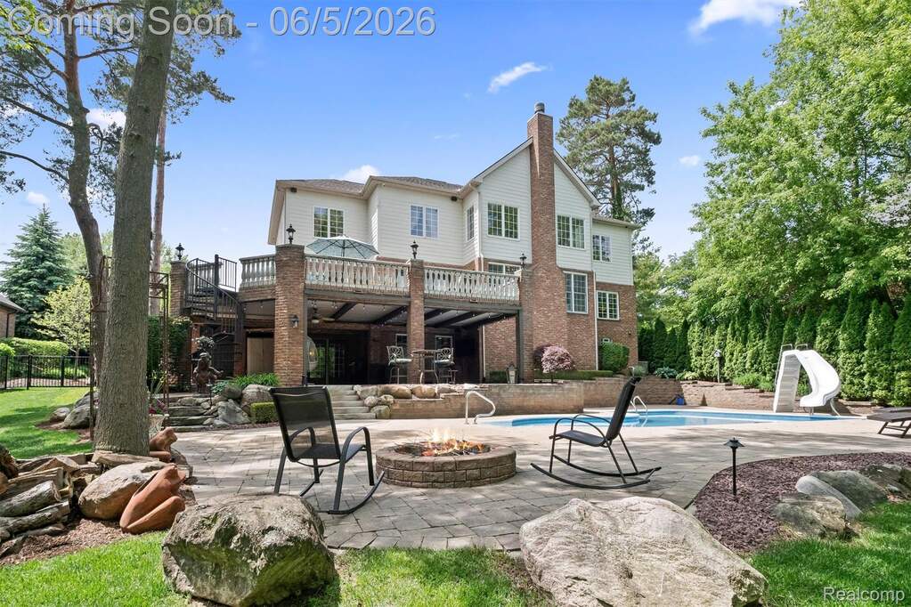 Expansive backyard featuring a paver patio with a built-in fire pit, an in-ground swimming pool with a slide, and a multi-level deck with a spiral staircase