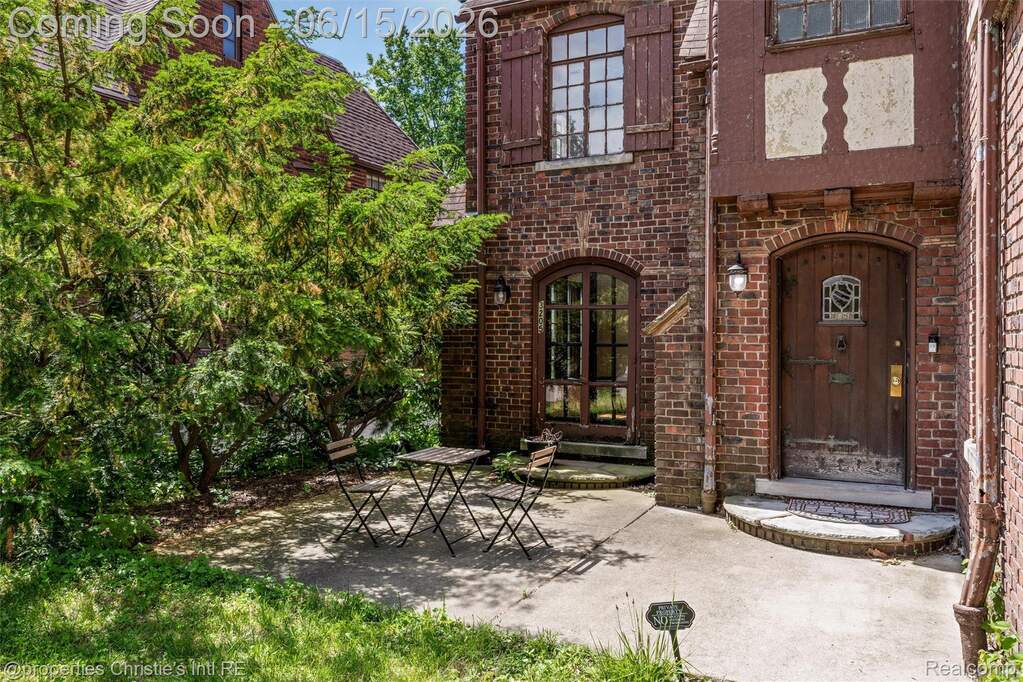 Brick exterior featuring an arched wood-paneled entry door with leaded glass detail, coordinating arched glass-paneled door, second-story casement window with exterior shutters, and concrete 