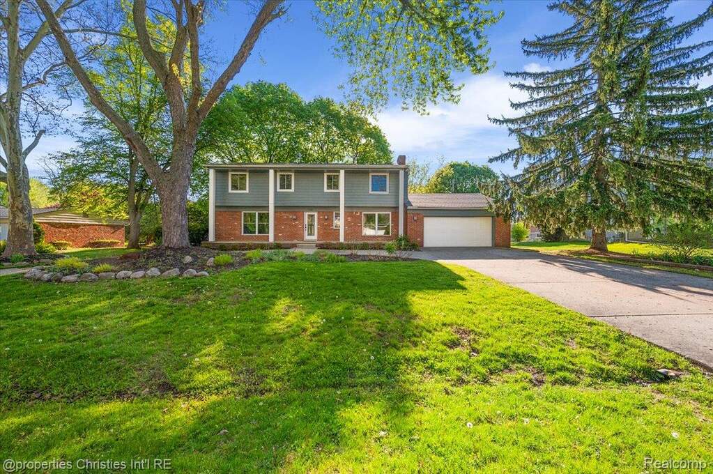 Colonial-style house with brick siding, an attached garage, a front yard, and driveway