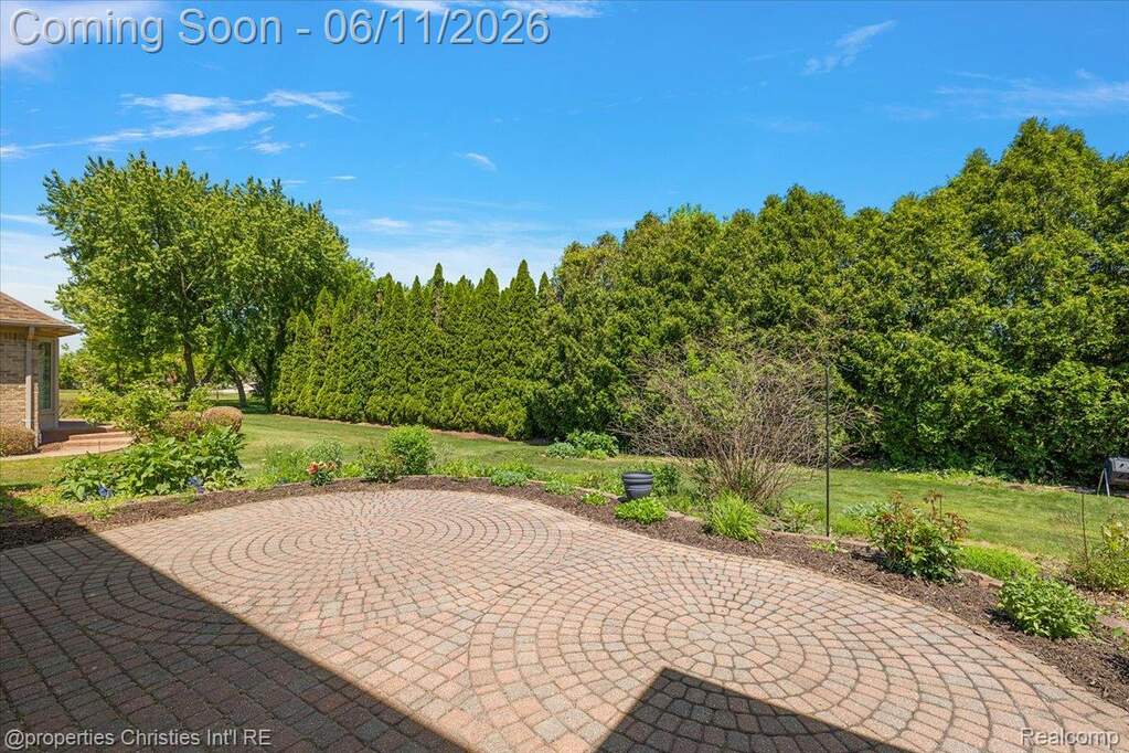 Expansive brick paver patio featuring a circular pattern, surrounded by a manicured lawn and mature privacy hedges