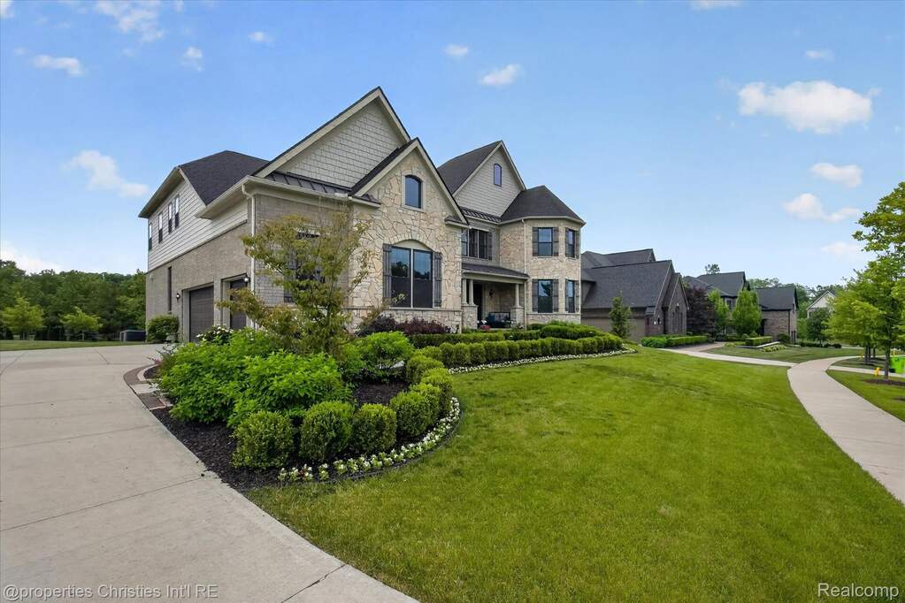 Stone and siding exterior featuring a multi-car garage, established front landscaping, front porch entry, and a paved driveway