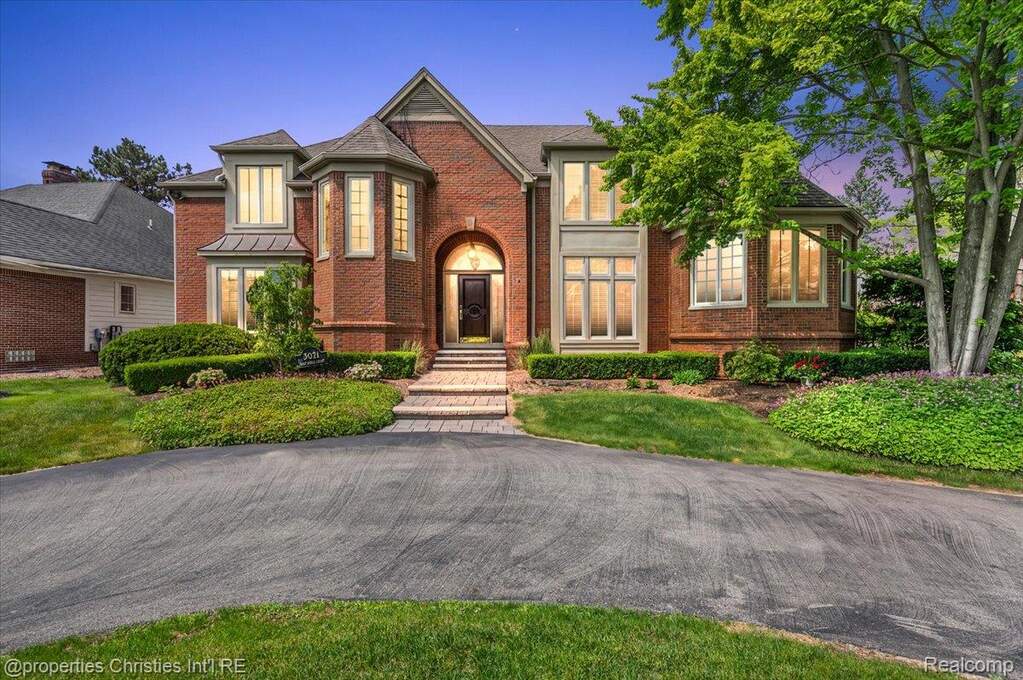 Stately brick-clad residence featuring a circular driveway, arched entryway, bay windows, and mature landscaping