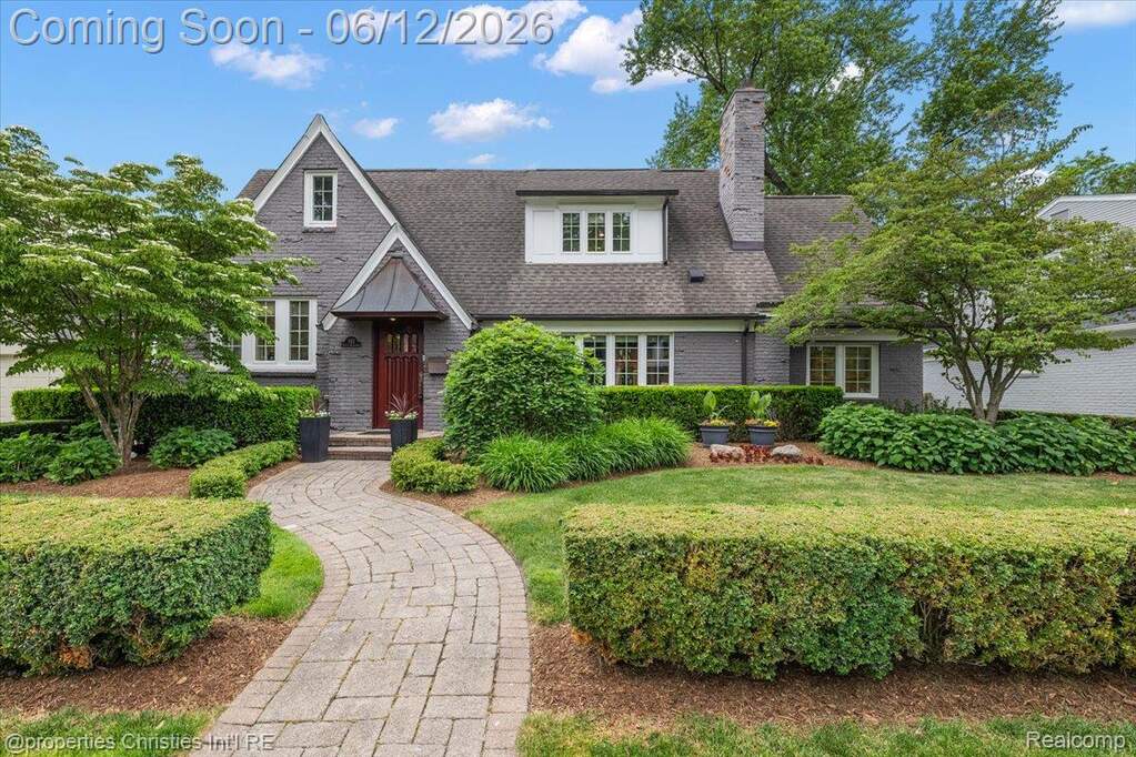 Traditional-style residence featuring a gray brick exterior, dark shingle roof, and white trim windows