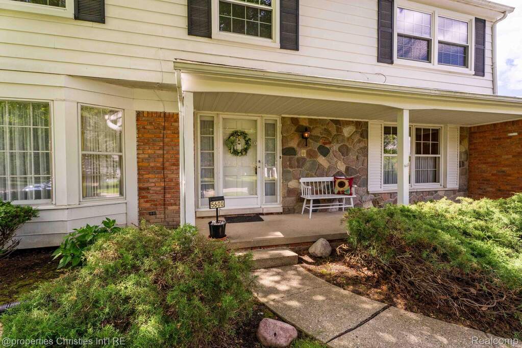 Front exterior featuring a covered porch with stone veneer accents, white siding, and a concrete walkway