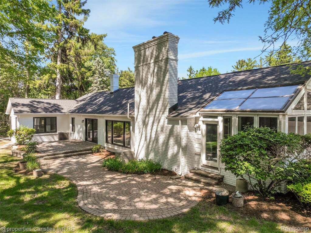 Exterior featuring a white brick facade, multiple large windows, a sunroom extension, a prominent brick chimney, and a circular paver patio