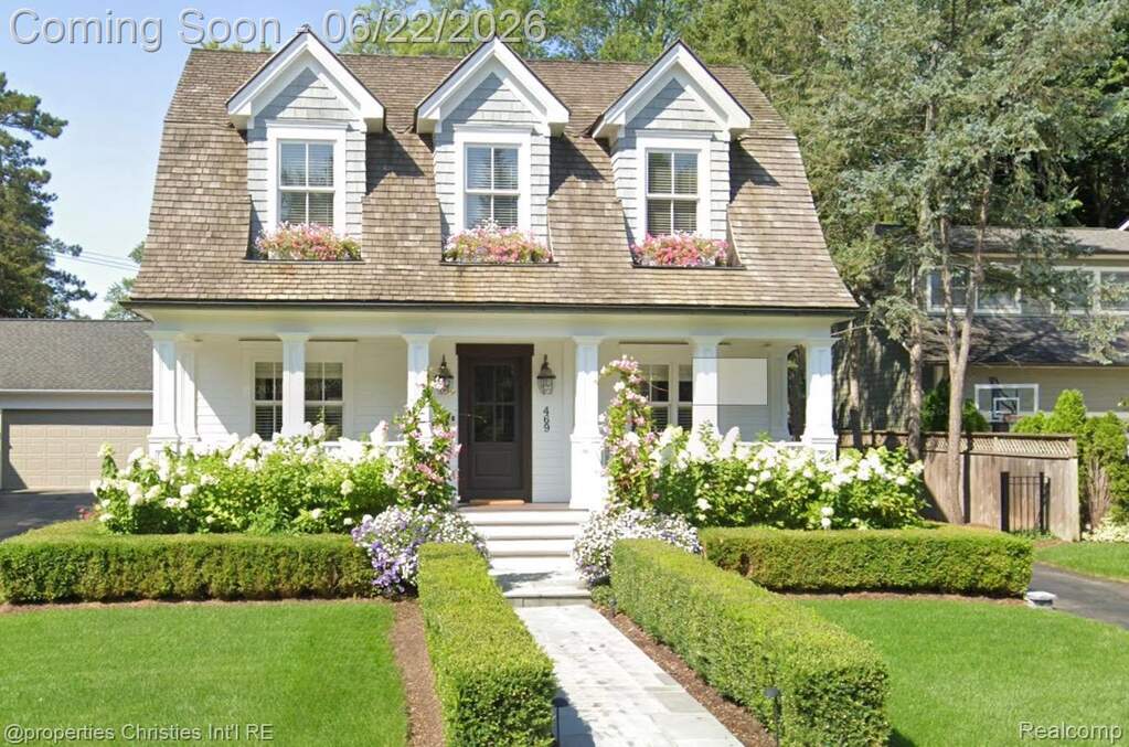 Dormer-style facade featuring shingle siding, a covered porch with white columns, and a dark wood entry door