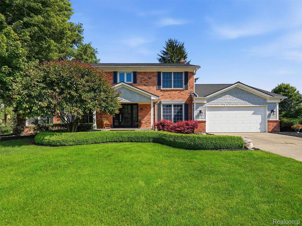 Brick and siding exterior featuring a two-car garage, mature landscaping, and a manicured lawn