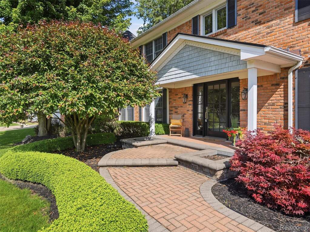 Brick facade residence with a covered entry featuring shingle siding and white columns
